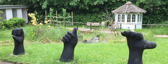 Foto fra en have med tre sorte skulpturer forestillende tegn fra håndalfabetet